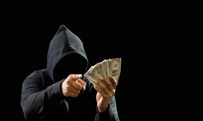 Fotobehang Portrait bandit man hacker one person wearing hood black shirt, sitting onchair and table thief hand holding money payment counting the amount obtained from hijacking or robbing, in dark background © Singh