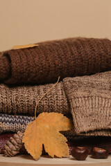 Pile of knitted wool sweaters with autumn dry leaves. Winter autumn cozy season concept.