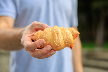 A man's hand holds a croissant, snack and fast food concept. Selective focus on hands with blurred background