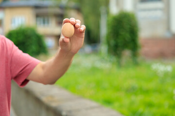 The guy's hand holds an egg. Selective focus on hands with blurred background