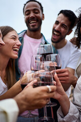 Vertical group multiracial excited friends toasting red wine and celebrating party outdoors. Young people together cheers on open air. Boys and girls enjoying free time on summer weekend vacation.