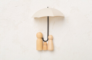 Umbrella and wooden family figures on concrete background, top view. Insurance coverage concept.