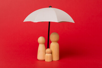 Wooden family figures with umbrella on color background