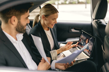 Business colleagues working with documents during video conference in back seat of car
