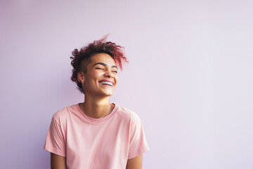 Young laughing gender non-binary person with pink dyed curly hair on a light pink background. Copy space. 
