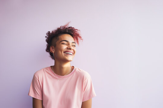 Young laughing gender non-binary person with pink dyed curly hair on a light pink background. Copy space.  - Powered by Adobe