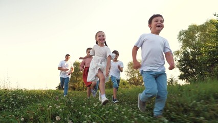 Smiling children with parents run across grassy field on family vacation