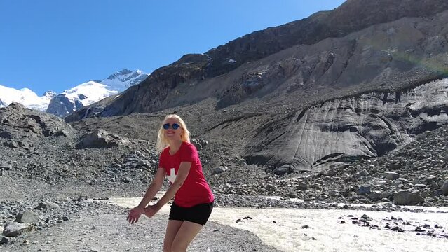Woman jumping in SLOW MOTION with red swiss flag t-shirt on the base of Morteratsch glacier of Switzerland. Bernina Range glacier of the Bundner Alps in Graubunden canton of Switzerland.