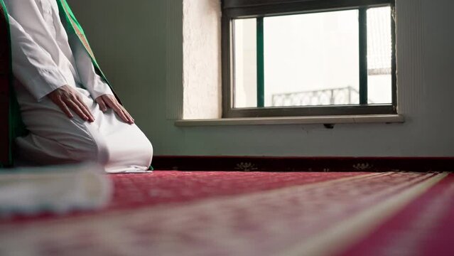 A Muslim believer prays in the twilight by a window in a mosque kneels down puts his forehead on carpet and turns to Allah
