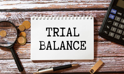 TRIAL BALANCE text on paper with magnifier, coffee and keyboard on grey background