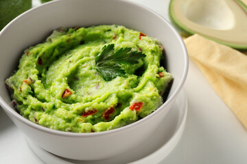 Bowl of delicious guacamole with parsley on white table, closeup