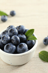 Bowl of fresh tasty blueberries with leaves on white wooden table, closeup. Space for text