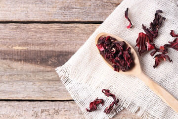 Spoon with dry hibiscus tea on wooden table, flat lay. Space for text © New Africa