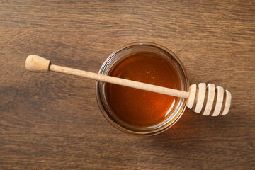 Dipper and jar with honey on wooden table, top view
