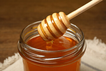 Pouring honey from dipper into jar at table, closeup