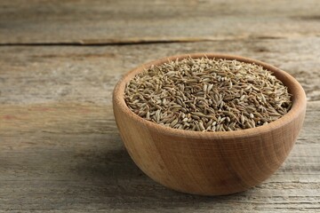 Bowl of caraway seeds on wooden table, closeup. Space for text