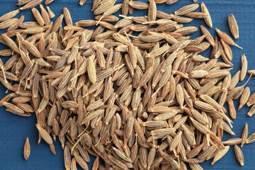 Pile of caraway seeds on blue wooden table, top view
