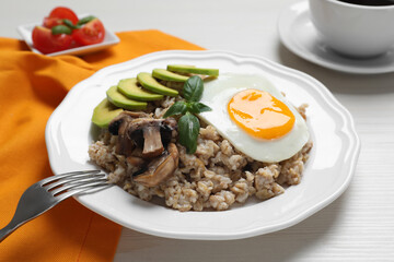 Tasty boiled oatmeal with fried egg, avocado and mushrooms served on white wooden table