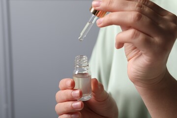 Woman with bottle of cosmetic serum and pipette on grey background, closeup. Space for text