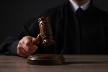 Judge with gavel sitting at wooden table against black background, closeup