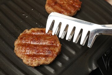 Taking delicious hamburger patty with tongs from grill pan, closeup