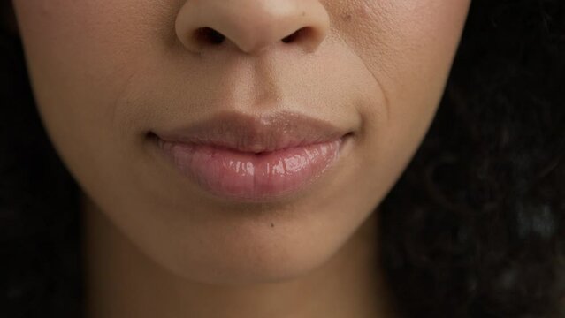 Sensual dark skinned woman sexually biting plump lips. Close up young woman face with perfect soft skin biting sexy pink lips and speaking.Attractive woman glossy lips with afro curly hair around face