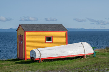 A small yellow and red colored wooden boatshed with a vintage white wooden fishing boat. The boat...