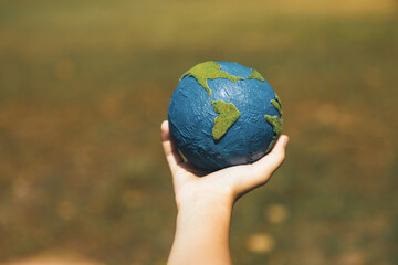 Young boy's hand holding planet Earth globe at natural park background as Earth day to save this planet with ESG principle and environment friendly energy for brighter future. Gyre