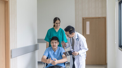 Obraz premium Young boy patient sitting on a wheelchair and getting support from nurse to go around. Handicapped patient uses wheelchair with support from physical therapist.