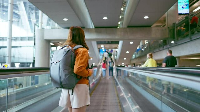 Young asian woman in international airport terminal or modern train station. Backpacker passenger female commuter walking on escalator