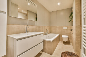a modern bathroom with white fixtures and beige tiles on the walls, along with a large mirror over...