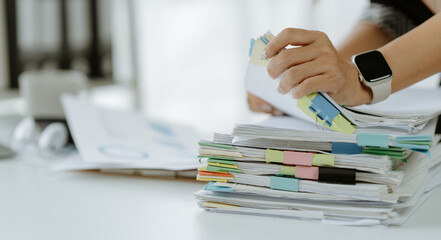 Businessman man working in stacks of papers searching for unfinished paperwork information on form check stack on table and checking financial papers in busy workload	