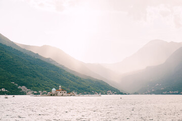 Island of Gospa od Skrpjela in the Bay of Kotor against the backdrop of mountains in the sunlight. Montenegro