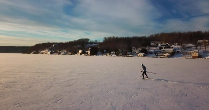 Panning Forward Shot Of Man Skiing On Frozen Portage Lake Against Sky At Sunset - Houghton, Michigan