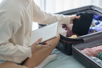 Fotobehang Asian girl preparing vacation in bedroom. Woman doing checklist © Charlie's