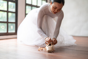 Ballerina in ballet shoes. Asian girl tying ribbons of toe shoes. ballet dancer preparing and...