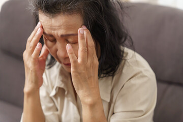 Sad middle age Asian woman touching forehead having headache suffering from migraine. mature asian woman feeling sick or depression.