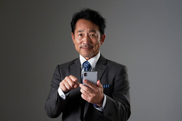 スマートフォンを使うビジネスマン　黒背景　カメラ目線