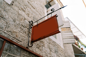 Empty tablet hangs on a forged signpost on the stone facade of an old house