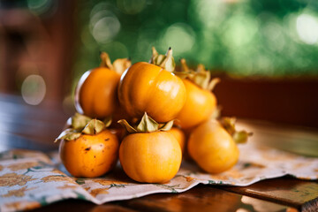 Pile of ripe persimmon lies on a colorful napkin on a wooden table