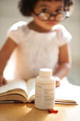 Obraz na płótnie Canvas Girl, child and reading or book pill bottle or adhd diagnosis, learning or development. Kid, glasses and childhood discipline story knowledge concentration, medical capsules or thinking at school