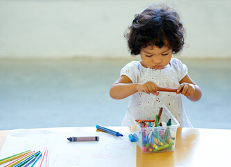 Young girl, crayons and drawing in classroom for creative development, education growth in...