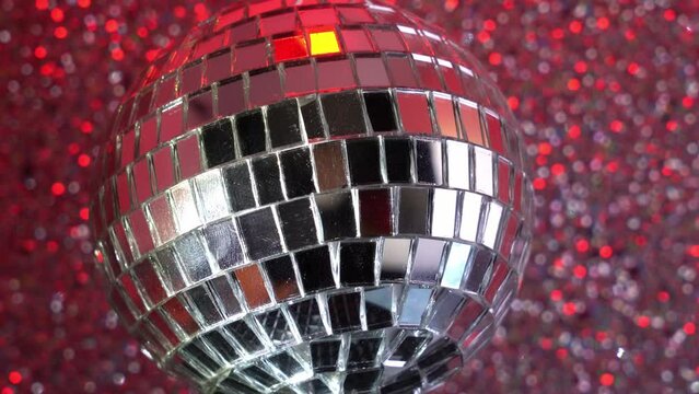 Close up footage of a small disco ball slowly rotating on a blur silver glitter background