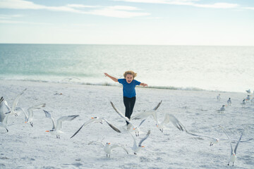 Excited kid running on beach. Child chasing birds near summer beach. Excited boy running on the beach with flying seagulls birds.