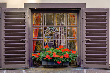 Fototapeta na wymiar Ornate stained glass window with wooden shutters and flowers on a traditional half timbered house in the historic center of Strasbourg, Alsace, France
