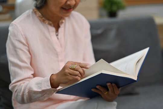 Close-up image of a Senior Asian woman reading a favorite book, literature, happy middle-aged female relaxing, enjoying free time, the weekend at home. Elderly people's lifestyles and leisure