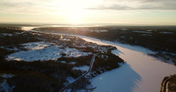 Aerial Descending Shot Of Frozen Lake Amidst Trees And Houses Against Sky At Sunset - Houghton, Michigan