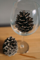 One cone is in a crystal wine glass, the second cone lies next to it on a wooden stand. The background is grey