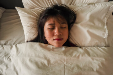 A beautiful Asian woman with long hair is sleeping soundly on a bed with a white pillow and blanket. Sleep comfortably at the hotel during holiday vacation. Rest after a long journey