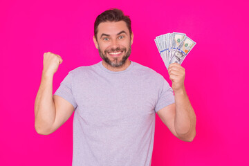 Man showing cash money in dollar banknotes. Portrait of business man isolated on pink studio background. Successful winner celebrating success or victory with money bills.